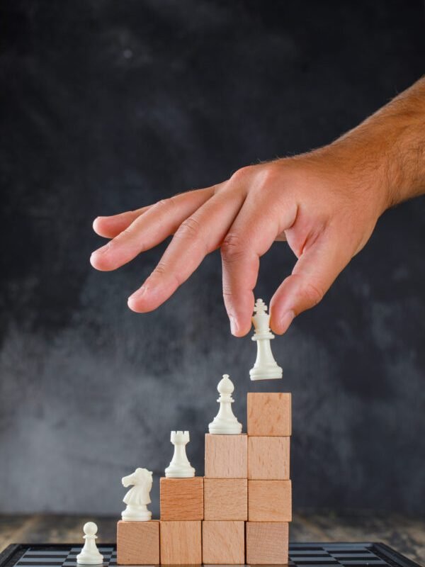Business success concept with chessboard on wooden and foggy background side view. man placing figure on pyramid of blocks.